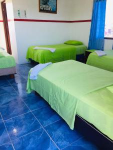 a room with three beds with green covers in it at Posada del Caminante in Puerto Villamil