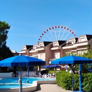 a ferris wheel and a swimming pool with blue umbrellas at B&C Apartments in Lido di Jesolo