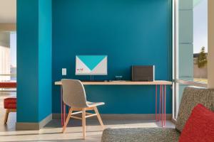 a desk with a chair and a computer on a blue wall at avid hotels - Prattville - Montgomery North, an IHG Hotel in Prattville