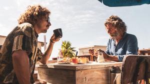 Zwei Männer sitzen mit einem Drink an einem Tisch. in der Unterkunft Piedra Alta Hostel & Suites in La Pedrera