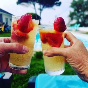 dos manos sosteniendo dos bebidas con una fresa en la parte superior en Furnaka Eco Village, en Lourinhã