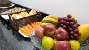 a bowl of fruit on a table with grapes and oranges at Hotel Carmelo in São José dos Pinhais