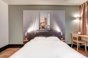 a bedroom with a large white bed and a desk at B&B HOTEL Louveciennes in Louveciennes