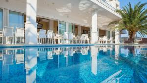 - une piscine avec des chaises blanches et un palmier dans l'établissement Hotel Perla, à Rogoznica