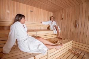 Duas mulheres estão sentadas numa sauna. em Castello Bonaria Wine & Spa Resort em Campiglia Marittima