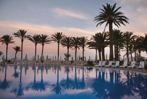 a swimming pool with palm trees and lounge chairs at Hotel Riu Palace Tres Islas in Corralejo