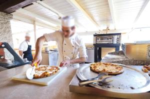 Un uomo in cucina che prepara due pizze su un bancone di SECRET VILLAGE Budoni a Budoni