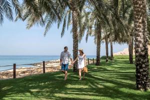 a couple walking along the beach with palm trees at Shangri-La Barr Al Jissah, Muscat in Muscat