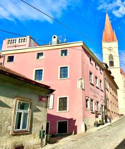 um edifício cor-de-rosa com uma torre de relógio numa rua em Boutique Apartments U Rolanda, Mikulášské náměstí em Znojmo