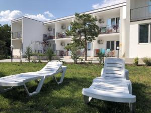 Deux chaises blanches assises dans l'herbe devant un bâtiment dans l'établissement Ассоль, à Kobleve