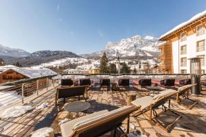 un patio con sillas, mesas y montañas de fondo en Grand Hotel Savoia Cortina d'Ampezzo, A Radisson Collection Hotel, en Cortina dʼAmpezzo