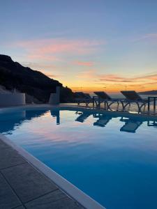 a pool with tables and a sunset in the background at Kokkinos Villas in Akrotiri