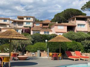 Le village de l'hacienda - Marina di santa Giulia- Porto-Vecchio في بورتو فيكيو: مجموعة من الكراسي والمظلات بجانب المسبح