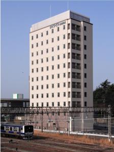 een wit gebouw met een trein ervoor bij Life Inn Katsuta Station West in Hitachinaka