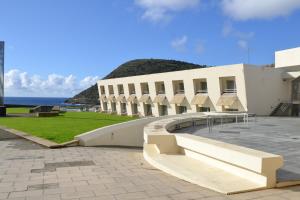 - un bâtiment blanc avec des bancs en face de l'océan dans l'établissement Pousada de Angra do Heroismo Castelo de S. Sebastiao, à Angra do Heroísmo