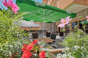 um pátio com um guarda-chuva verde, mesas e flores em AlpenParks Hotel & Apartment Hochkönig em Mühlbach am Hochkönig