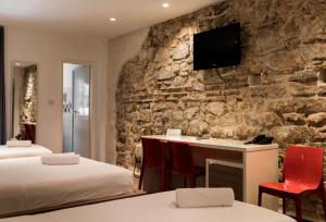 a bedroom with two beds and a desk with a tv on a stone wall at Slavija Culture Heritage Hotel in Split