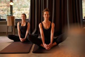 Dos mujeres sentadas en una pose de yoga en una habitación en THE HEARTS HOTEL - dein Boutique- und Event-Resort, en Braunlage