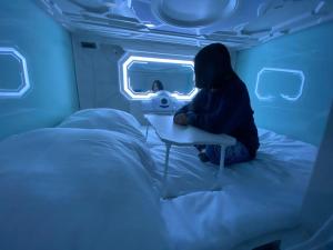 Space Night Capsule Hostel في برلين: شخص يجلس على سرير في غرفة زرقاء