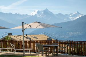 een tafel en stoelen en een parasol op een terras met bergen bij Hotel Ad'Eldorado in Crans-Montana