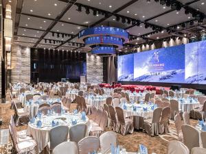 um salão de banquetes com mesas e cadeiras brancas e um ecrã em Vienna International Hotel Foshan The World of Flowers em Shunde