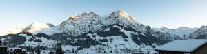 eine schneebedeckte Bergkette mit einem Gebäude im Vordergrund in der Unterkunft Hotel Viktoria Eden in Adelboden