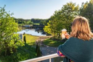 une femme assise sur une balustrade tenant une tasse de café dans l'établissement Hotel Kiston, à Sulęczyno