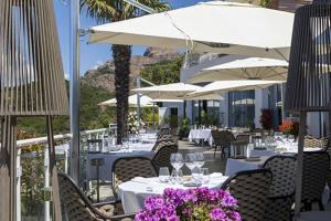 um restaurante com mesas, guarda-sóis brancos e flores roxas em Hôtel Capo Rosso em Piana