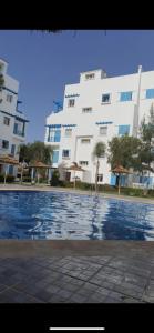 Smir Park appartement Haut standing Marina Smir في مارينا سمير: مبنى ابيض كبير امامه مسبح