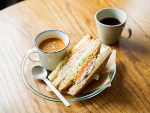 un sándwich en un plato junto a dos tazas de café en ROUTE - Cafe and Petit Hostel, en Nagasaki