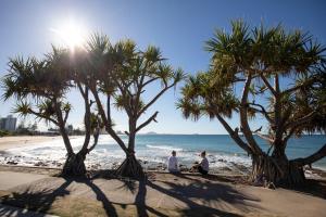 due persone sedute sulla spiaggia tra le palme di Alex Beach Cabins and Tourist Park ad Alexandra Headland