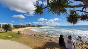 Due persone sedute su un muro che guardano la spiaggia di Alex Beach Cabins and Tourist Park ad Alexandra Headland