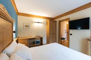 a bedroom with a bed and a desk with a television at Hotel Medil in Campitello di Fassa