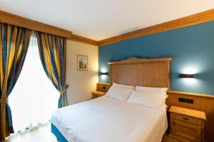 a bedroom with a white bed and a blue wall at Hotel Medil in Campitello di Fassa