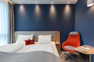 レーゲンスブルクにあるHoliday Inn Express - Regensburg, an IHG Hotelのベッドと赤い椅子が備わるホテルルームです。