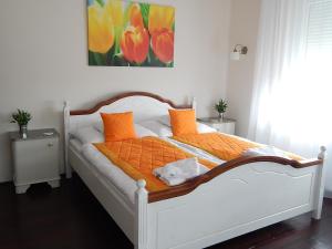 a white bed with orange pillows and a painting on the wall at Bogácsa Apartman in Bogács