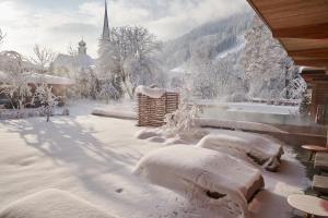 podwórko pokryte śniegiem z kościołem w tle w obiekcie MalisGarten Green Spa Hotel w mieście Zell am Ziller