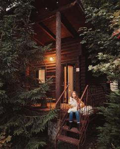 uma jovem sentada nas escadas de uma cabana de madeira em KLEN Family em Mykulychyn