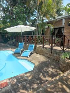 a pool with two chairs and an umbrella at African Dreamz Guest House in St Lucia