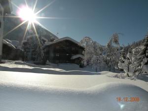 a snow covered yard with a building with the sun shining at Hotel Bellevue in Champoluc