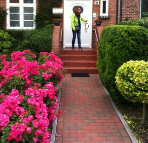 una mujer parada en la puerta principal de una casa con flores rosas en Stadthaus Jürgensby, en Flensburg