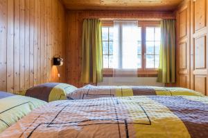 two beds in a room with wooden walls and a window at Chalet Sunnegga in Fiesch