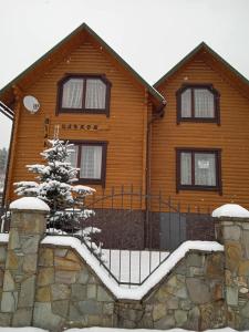 a wooden house with a fence and a snow covered tree at Вілла Олекси in Skhidnitsa