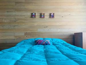 Una gran cama azul en una habitación con una pared de madera. en Casa Apel Hostel, en Puerto Varas