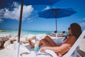 a woman sitting in a chair on the beach with a drink at Siboney Beach Club in Saint Johnʼs