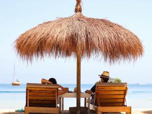 duas pessoas sentadas debaixo de um guarda-sol na praia em Hotel Islabela Islas Del Rosario em Isla Grande