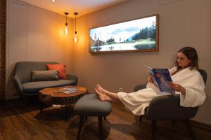 une femme assise sur une chaise en lisant un livre dans l'établissement Hotel Caprice - Grindelwald, à Grindelwald