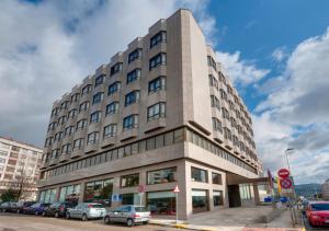 Un grand bâtiment avec des voitures garées devant lui dans l'établissement Hotel Vigo Los Galeones Affiliated by Meliá, à Vigo