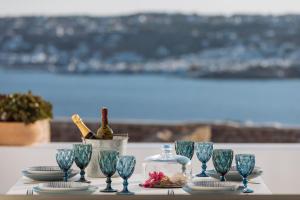 Villa Conza Mykonos في أغيوس يوانيس ميكونوس: طاولة مع كؤوس زرقاء وزجاجة من النبيذ