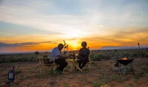 mężczyzna i kobieta siedzący przy stole przed zachodem słońca w obiekcie Amanya Double Pitch Tent with Mt Kilimanjaro View w mieście Amboseli